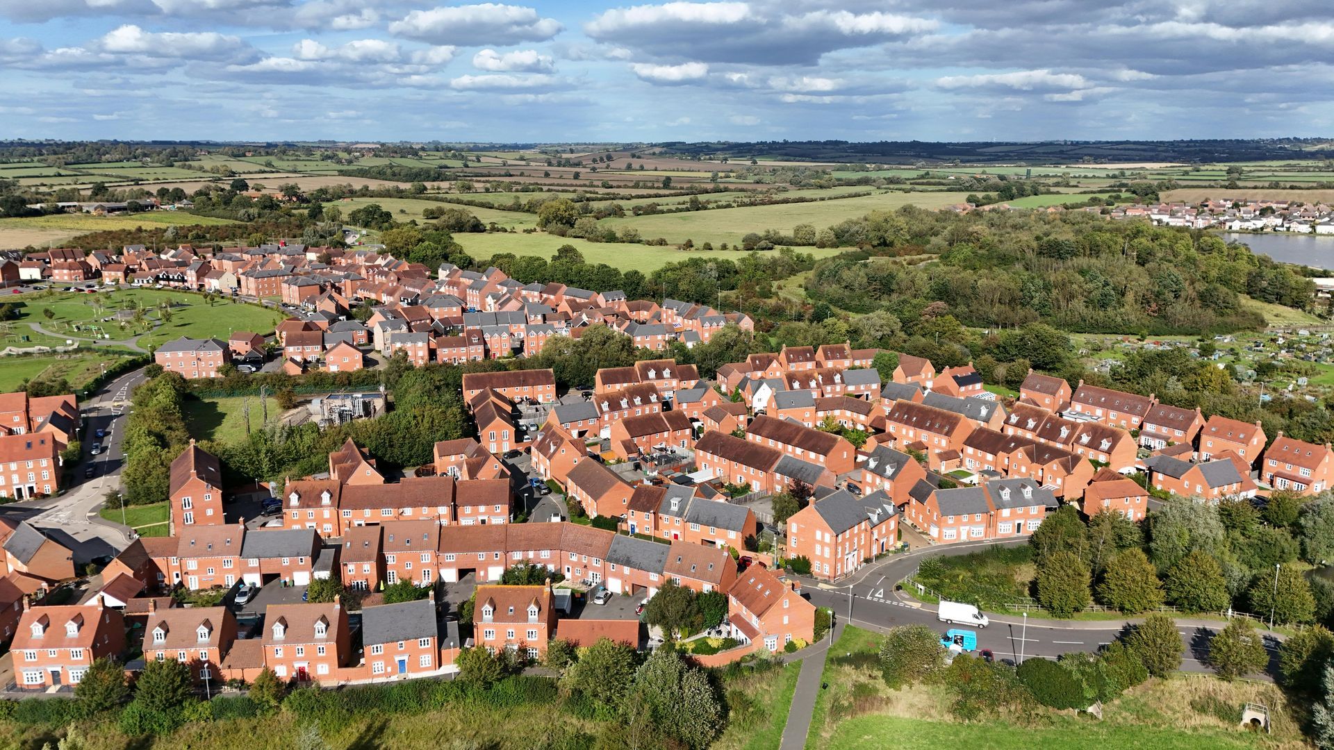 Aerial drone view of a modern residential housing estate with red brick houses and green surroundings under a blue sky